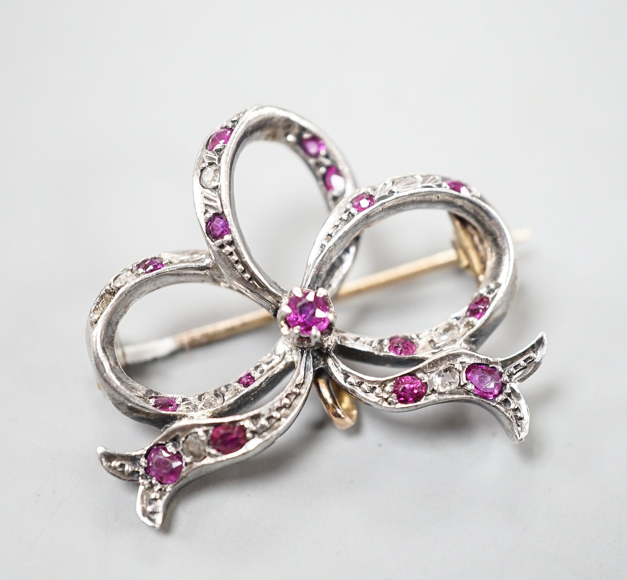 An early 20th century yellow metal, diamond and ruby set ribbon bow brooch, 31mm, gross 7.2 grams.